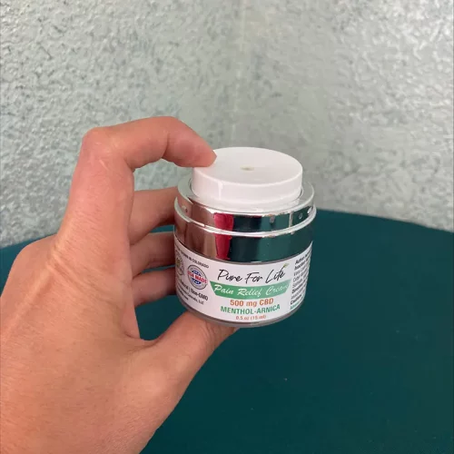 A jar of CBD oil cream in the hand of a healthy person