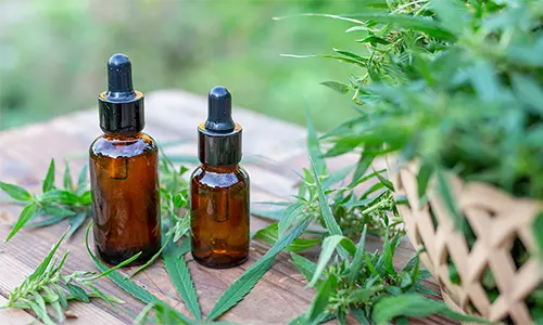 2 CBD bottles on a wooden table surrounded by hemp leaves