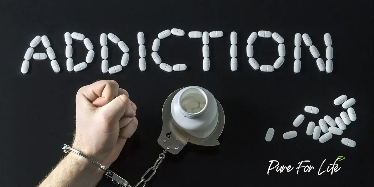 a hand in handcuffs with an open bottle with pills on a black background with many other while pills spread around in substance addiction letters